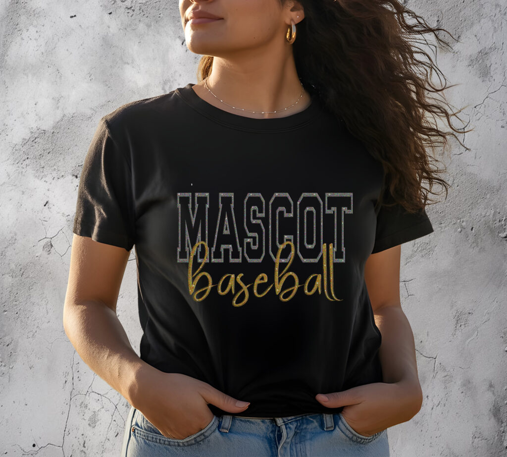 Woman wearing stylish black "Mascot Baseball" t-shirt with gold and white lettering, standing against a textured gray wall