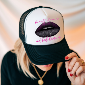 Trucker hat featuring a bold graphic of purple and black patterned lips with the phrase “beauty, brains and bad decisions.