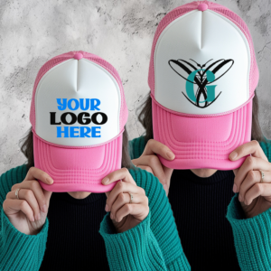 Two pink and white customizable trucker hats shown on a person, one with placeholder text “Your Logo Here” and the other with a custom monogram design.