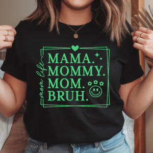 Woman wearing a black crew neck t-shirt with bright green graphic print reading Mama Mommy Mom Bruh in bold lettering inside a decorative bordered frame with a heart, sparkle stars, flowers, and smiley face accent icons