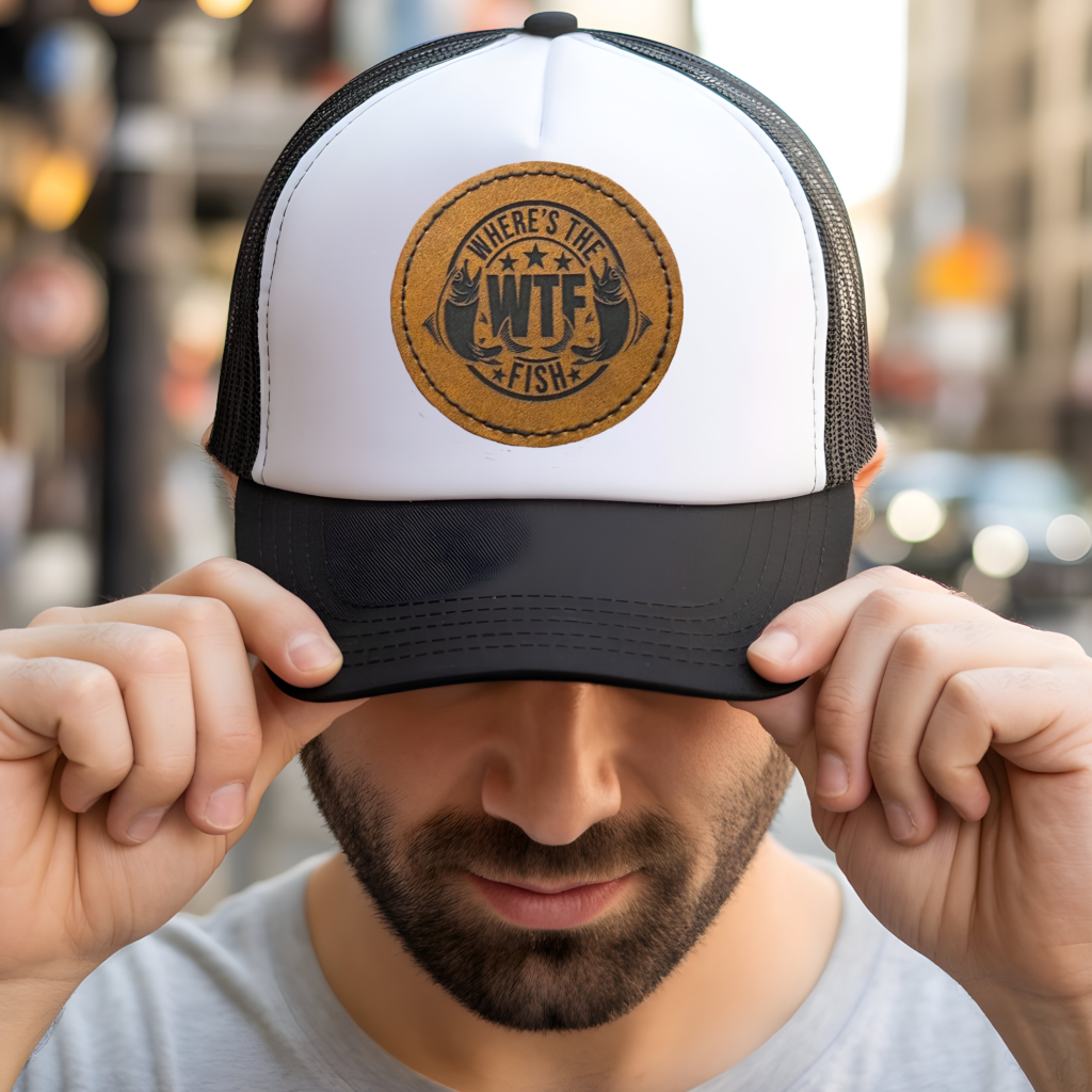 White and black trucker hat with round brown leather patch engraved with WTF Where's the Fish design featuring two fish and stars