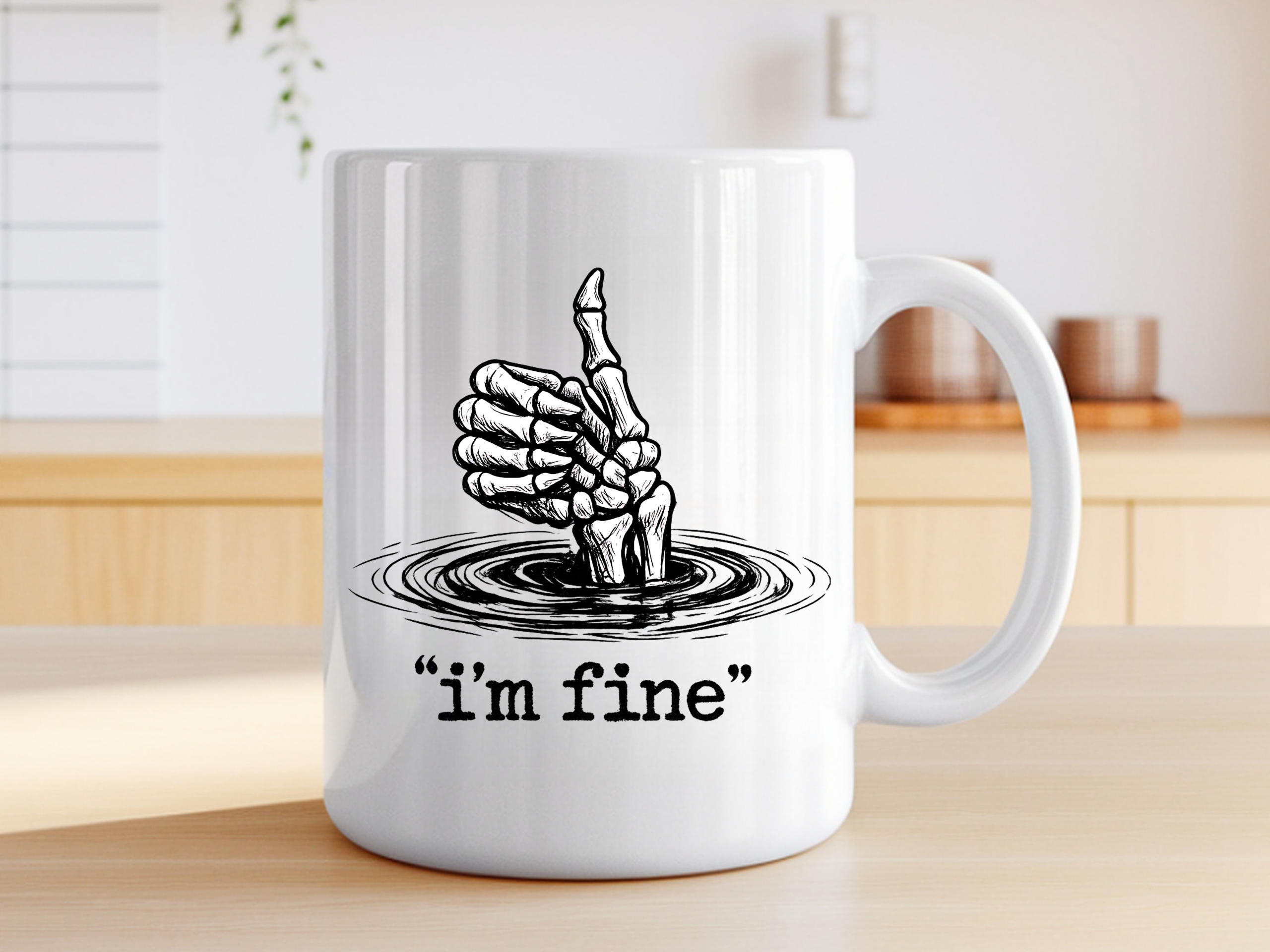 White ceramic coffee mug featuring a skeletal hand giving a thumbs up while sinking into water, with the text "i'm fine" in quotation marks on a on table.