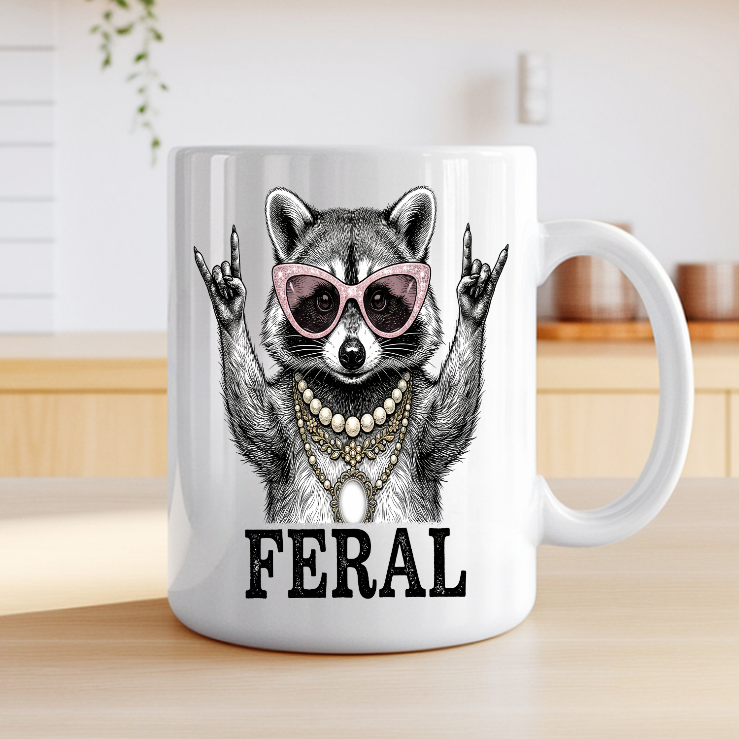 White ceramic coffee mug featuring a illustrated raccoon wearing pink cat-eye sunglasses and layered pearl and gold necklaces, throwing rock-on hand signs, with the word "FERAL" in bold text — on a table