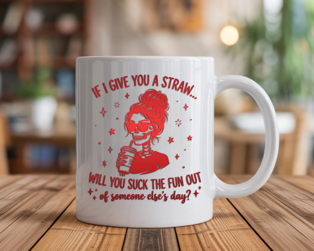 White coffee mug featuring a red gradient skull woman with sunglasses holding a coffee cup, surrounded by stars, with the text "If I give you a straw... will you suck the fun out of someone else's day?" displayed on a wooden table